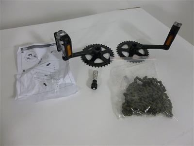 Two black bicycle cranksets with orange pedals, a bag of chain, a small tool, and instruction sheets on a white surface.